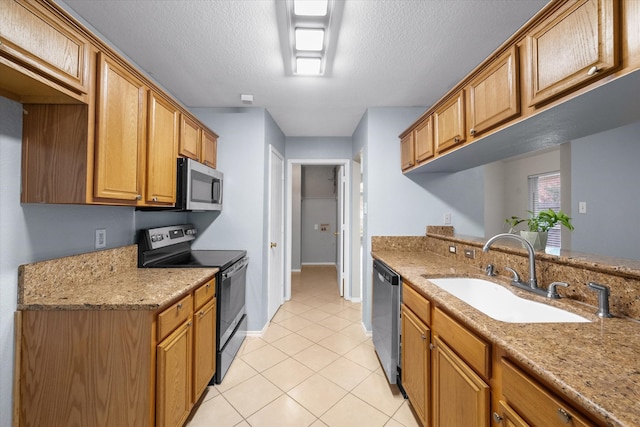 kitchen with a textured ceiling, appliances with stainless steel finishes, light stone counters, light tile patterned floors, and sink