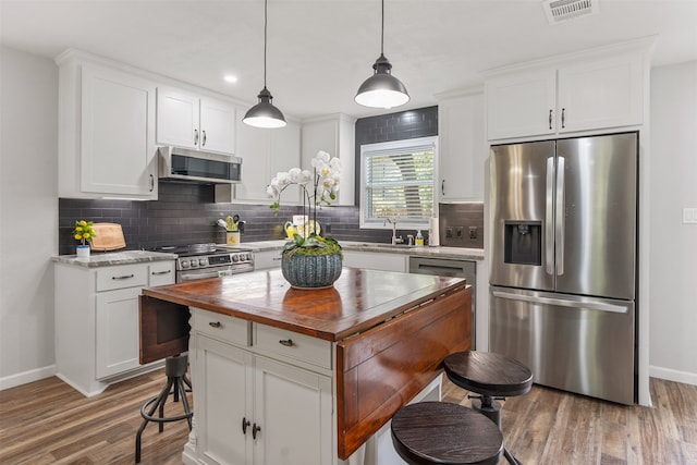 kitchen featuring hardwood / wood-style floors, backsplash, appliances with stainless steel finishes, butcher block counters, and a kitchen island