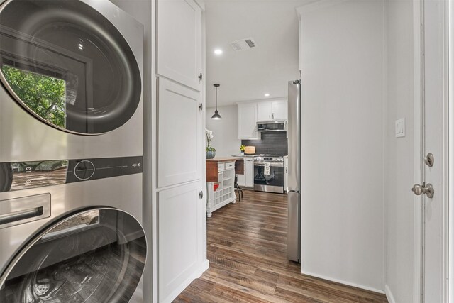 laundry area featuring dark hardwood / wood-style floors, stacked washer and clothes dryer, and cabinets