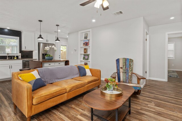 living room with ceiling fan, sink, dark wood-type flooring, and built in shelves