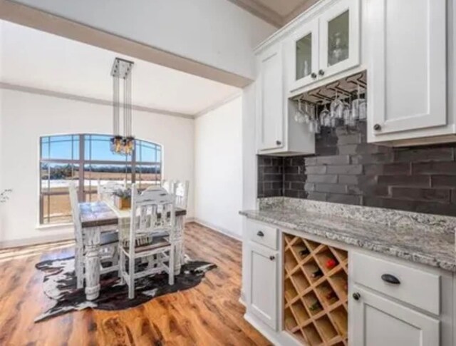 interior space with light stone counters, white cabinets, ornamental molding, backsplash, and light wood-type flooring