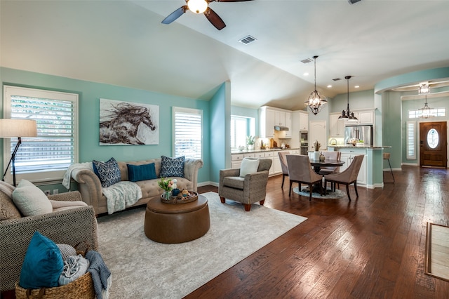 living room featuring ceiling fan with notable chandelier, dark wood-type flooring, and vaulted ceiling