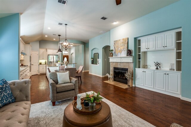 living room featuring vaulted ceiling, dark wood-type flooring, a tile fireplace, and an inviting chandelier