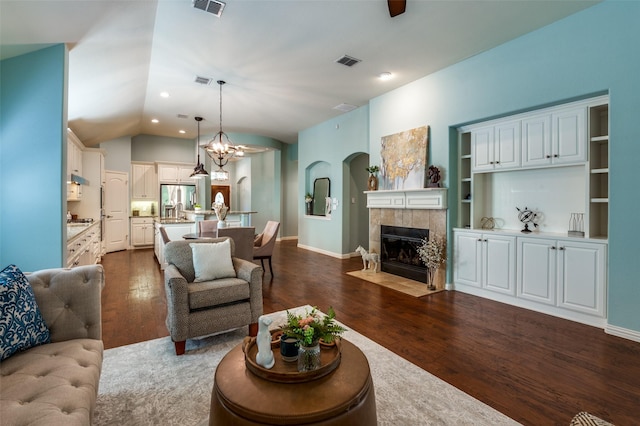 living area with dark wood-style floors, visible vents, vaulted ceiling, and a tiled fireplace