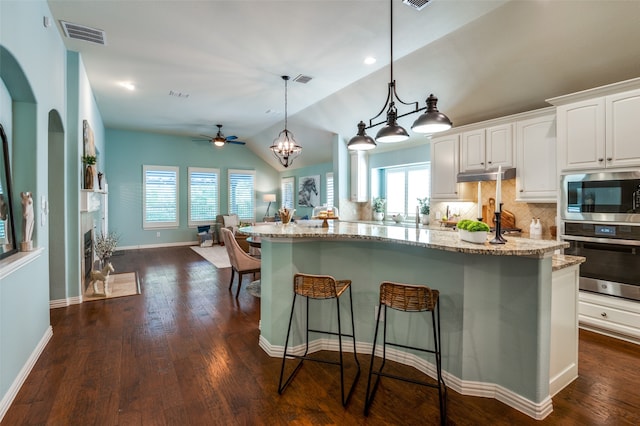 kitchen with dark hardwood / wood-style floors, appliances with stainless steel finishes, a breakfast bar area, backsplash, and white cabinetry