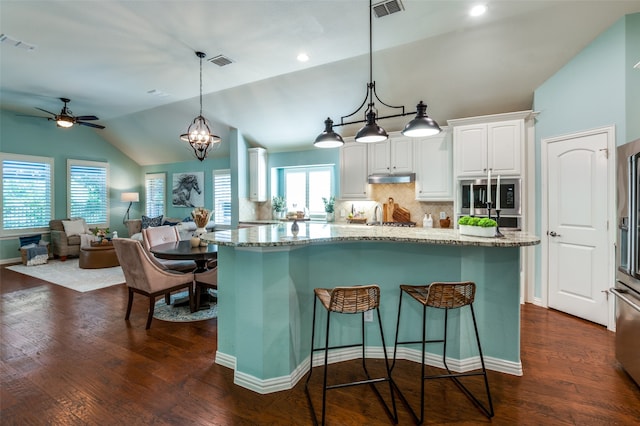 kitchen with dark wood-type flooring, light stone countertops, a breakfast bar, backsplash, and white cabinetry