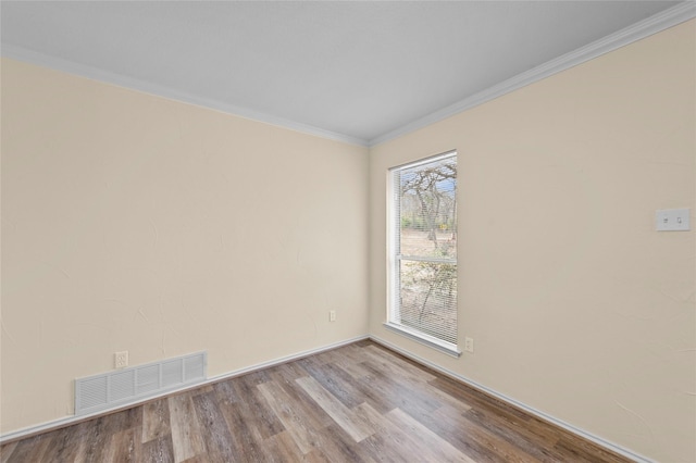 empty room featuring crown molding, baseboards, wood finished floors, and visible vents