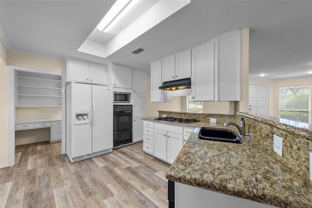 kitchen featuring visible vents, under cabinet range hood, a sink, dark stone countertops, and stainless steel appliances