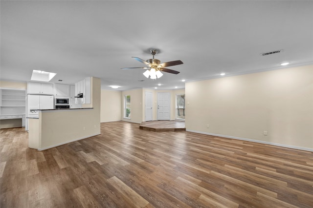 unfurnished living room featuring wood-type flooring, a skylight, crown molding, and ceiling fan