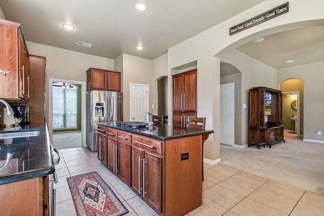 kitchen featuring dark stone countertops, stainless steel appliances, light colored carpet, sink, and a center island