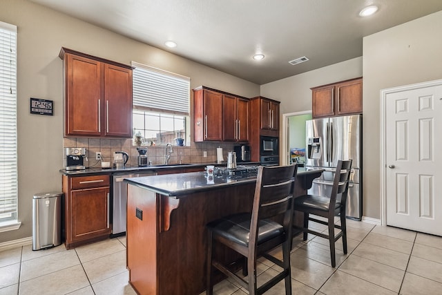 kitchen with decorative backsplash, light tile patterned flooring, a kitchen breakfast bar, a center island, and stainless steel appliances