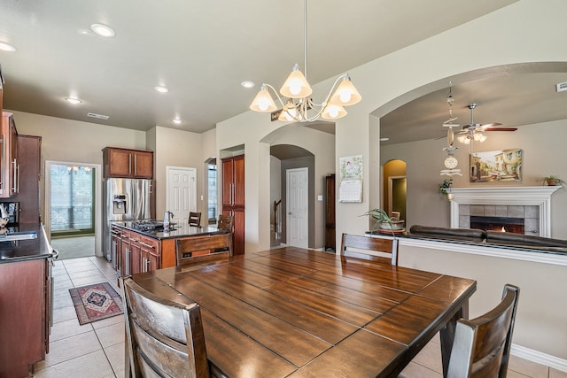 dining area with a tile fireplace, light tile patterned flooring, sink, and ceiling fan with notable chandelier