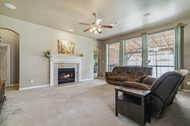 carpeted living room with ceiling fan, a textured ceiling, and a tile fireplace