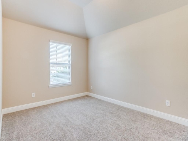 carpeted empty room featuring vaulted ceiling and baseboards