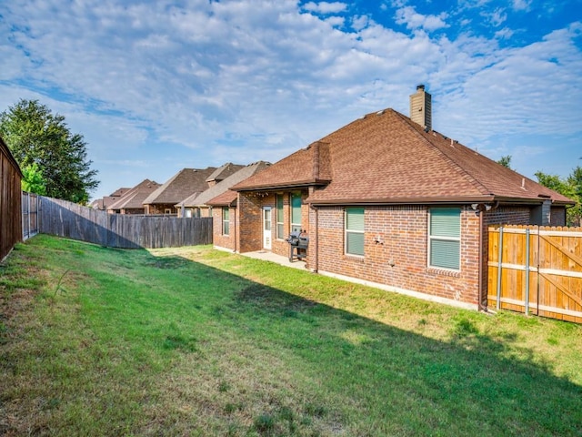 rear view of property with roof with shingles, a fenced backyard, a chimney, a lawn, and brick siding