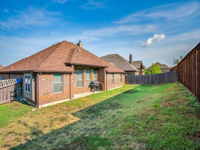 back of property with brick siding, a lawn, a chimney, and a fenced backyard