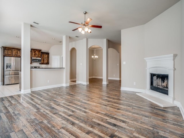 unfurnished living room featuring visible vents, a fireplace with raised hearth, ceiling fan with notable chandelier, arched walkways, and light wood-style floors