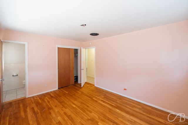 unfurnished bedroom featuring a closet, connected bathroom, and light hardwood / wood-style floors