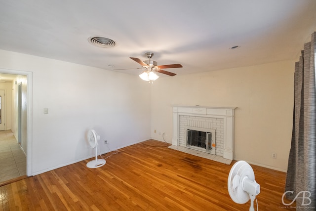 unfurnished living room featuring ceiling fan, light wood-type flooring, and a brick fireplace