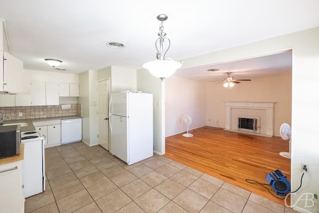 kitchen featuring tasteful backsplash, white appliances, light wood-type flooring, a brick fireplace, and white cabinets