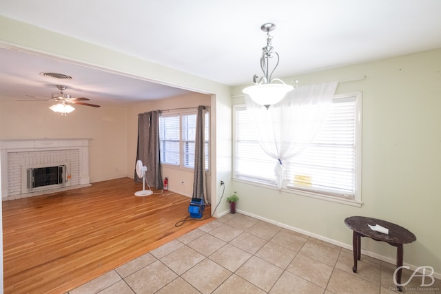 interior space with ceiling fan, light tile patterned floors, and a brick fireplace