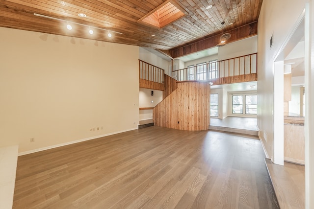 unfurnished living room with wood ceiling, a high ceiling, hardwood / wood-style flooring, and a skylight