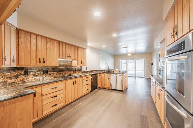 kitchen featuring tasteful backsplash, light brown cabinetry, stainless steel appliances, dark stone counters, and light hardwood / wood-style flooring