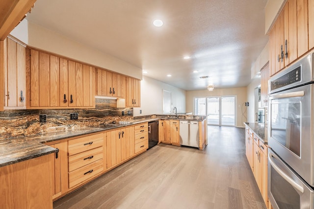 kitchen featuring light wood-style flooring, appliances with stainless steel finishes, decorative backsplash, dark stone counters, and light brown cabinetry