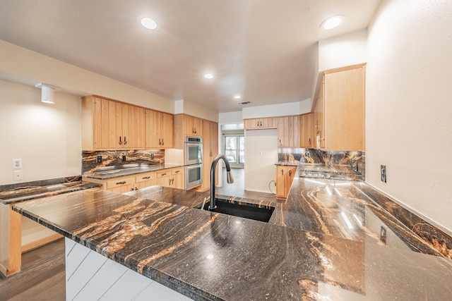 kitchen with light brown cabinets, kitchen peninsula, decorative backsplash, sink, and stainless steel double oven