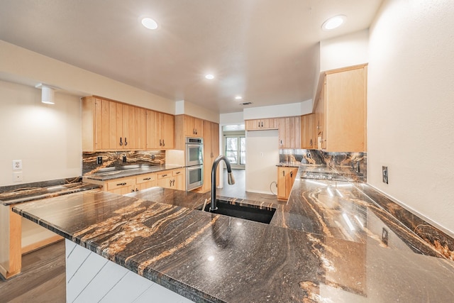 kitchen with double oven, light brown cabinets, a peninsula, a sink, and backsplash