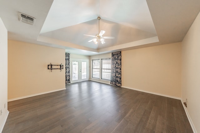 empty room featuring dark wood-type flooring, ceiling fan, a raised ceiling, and french doors