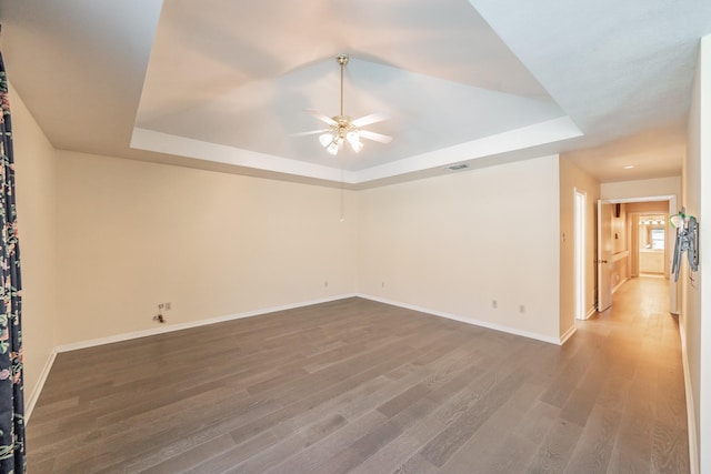 unfurnished room featuring ceiling fan, wood finished floors, visible vents, baseboards, and a raised ceiling