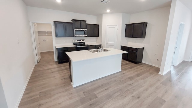 kitchen with light hardwood / wood-style floors, a kitchen island with sink, sink, and stainless steel appliances