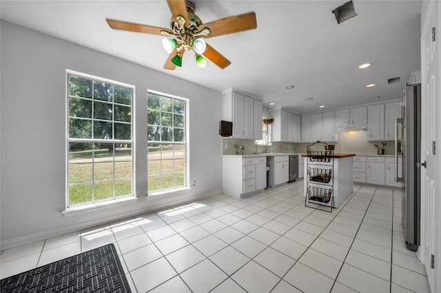 kitchen with stainless steel dishwasher, light tile patterned flooring, under cabinet range hood, and a sink