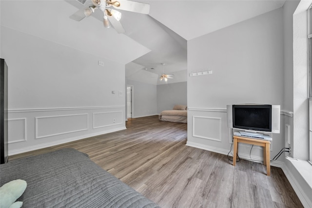 living area with wood finished floors, lofted ceiling, ceiling fan, and a decorative wall