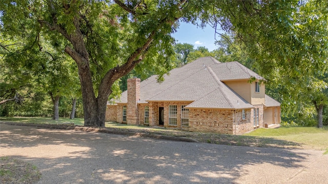 view of front of home featuring brick siding, a chimney, roof with shingles, and a front yard