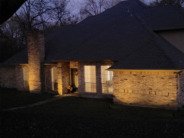 view of side of property with brick siding, a chimney, and roof with shingles