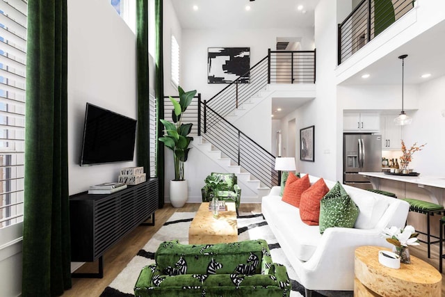 living room featuring a towering ceiling, stairs, wood finished floors, and recessed lighting