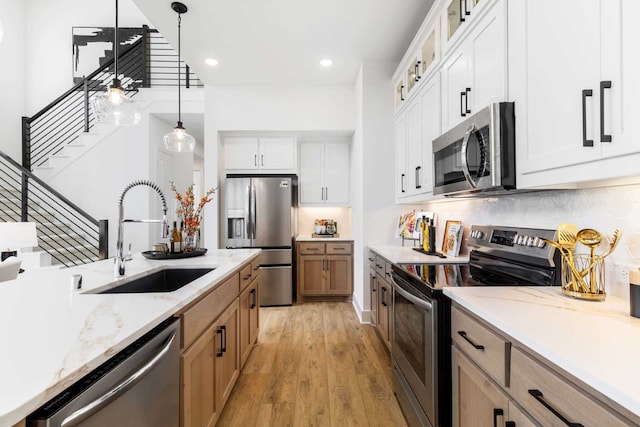 kitchen featuring glass insert cabinets, stainless steel appliances, a sink, light wood-style floors, and decorative light fixtures