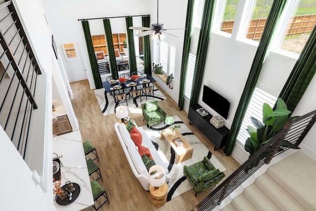 living area with stairs, a ceiling fan, light wood-style flooring, and baseboards