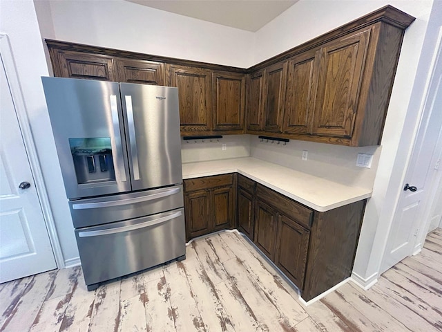 kitchen with dark brown cabinets, stainless steel refrigerator with ice dispenser, light countertops, and light wood-style floors