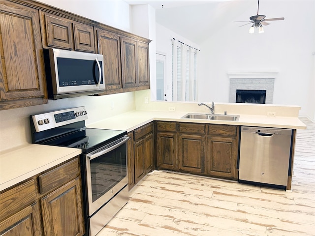 kitchen featuring sink, lofted ceiling, kitchen peninsula, stainless steel appliances, and a stone fireplace