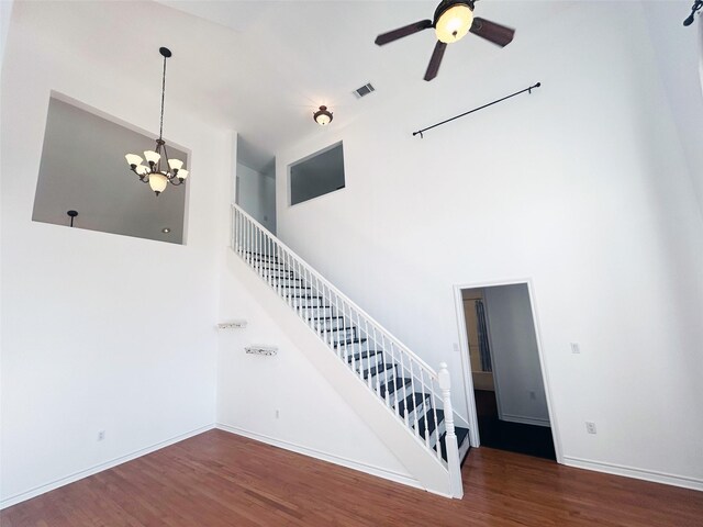 stairs featuring hardwood / wood-style flooring, ceiling fan with notable chandelier, and a high ceiling