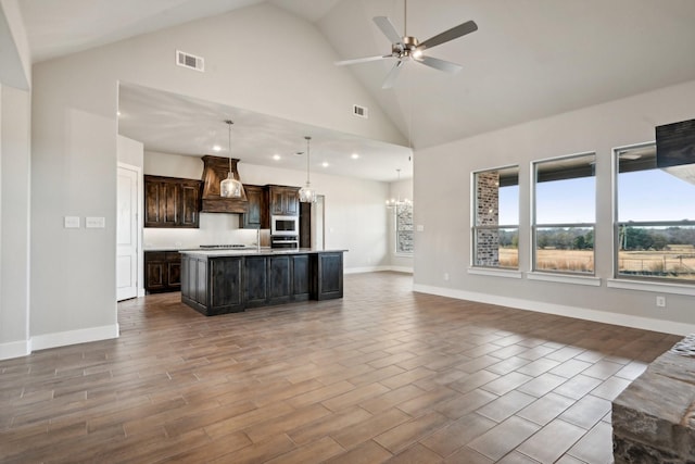 kitchen featuring ceiling fan with notable chandelier, pendant lighting, premium range hood, a kitchen island with sink, and dark brown cabinets