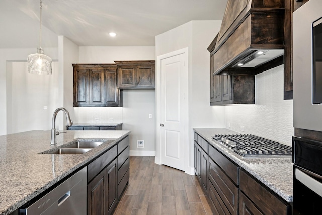 kitchen featuring premium range hood, appliances with stainless steel finishes, hanging light fixtures, light stone countertops, and sink