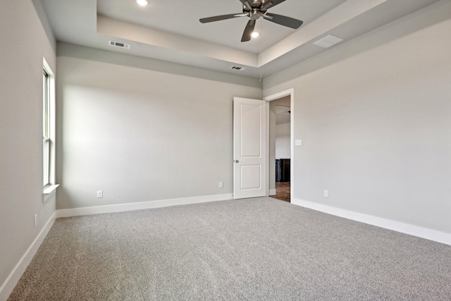 carpeted empty room featuring ceiling fan and a raised ceiling