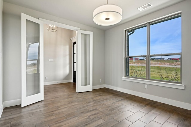 unfurnished room featuring french doors and an inviting chandelier