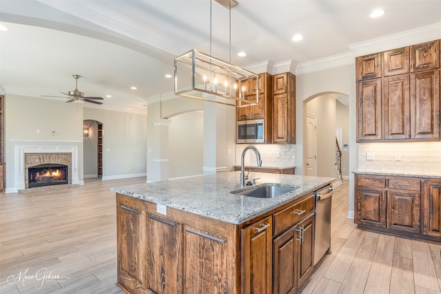 kitchen featuring appliances with stainless steel finishes, hanging light fixtures, light wood-type flooring, a center island with sink, and sink