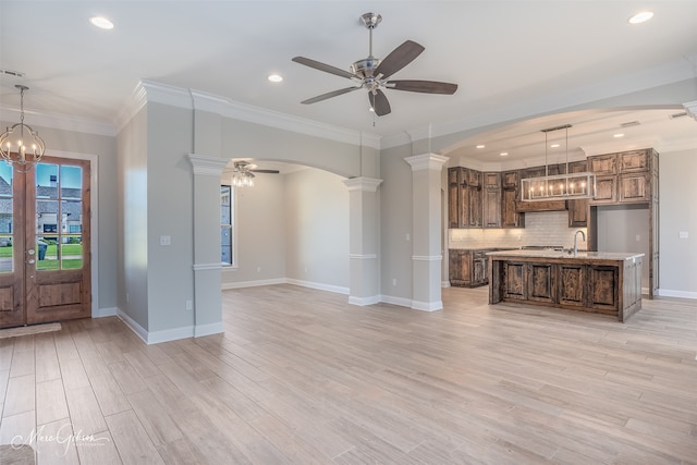 interior space featuring a center island with sink, decorative columns, light hardwood / wood-style flooring, and decorative light fixtures