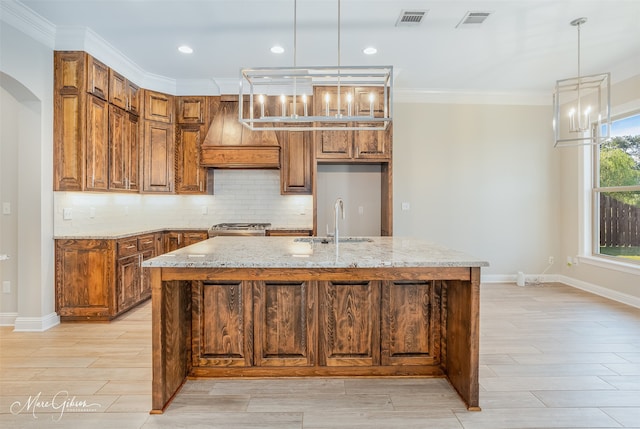 kitchen featuring custom range hood, a healthy amount of sunlight, a kitchen island with sink, and light stone counters